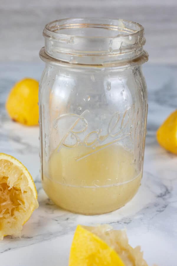 Lemon juice in glass mason jar with freshly squeezed lemons.