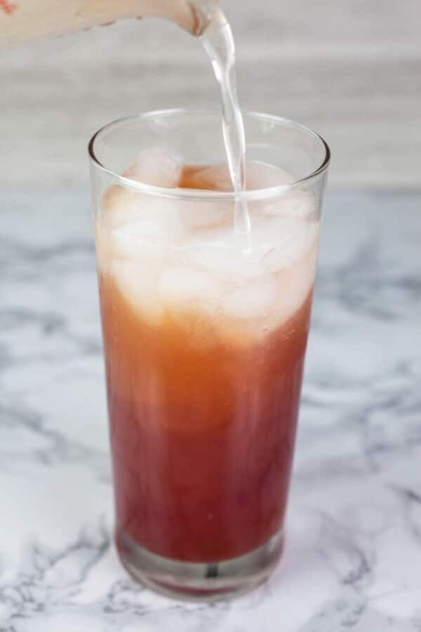 Ginger beer poured into highball glass with cranberry juice and apple cider.