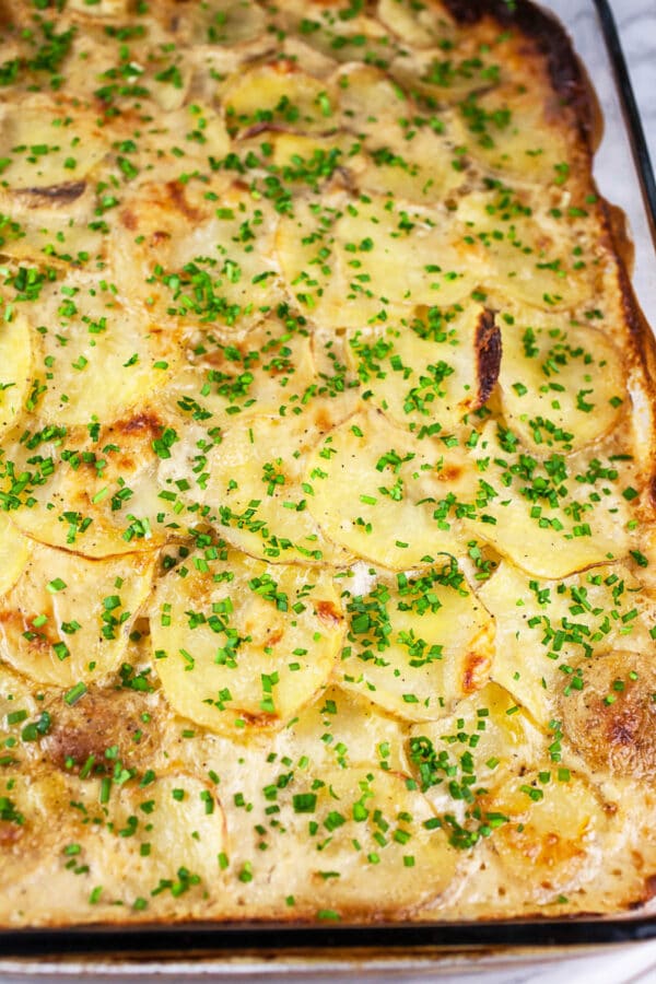 Baked au gratin potatoes topped with minced chives in glass cake pan.