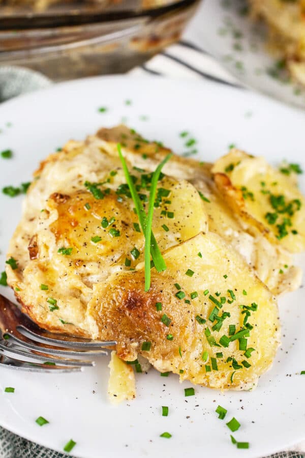 Gluten free au gratin potatoes with minced chives on small white plate.