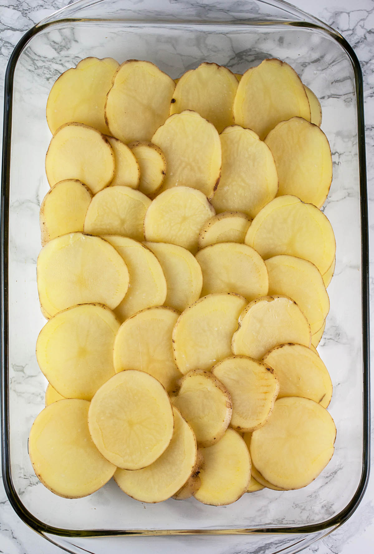 Thinly sliced yellow potatoes in glass cake pan.