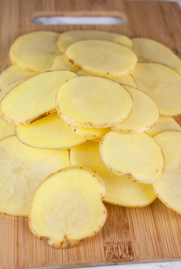 Thinly sliced yellow potatoes on wooden cutting board.