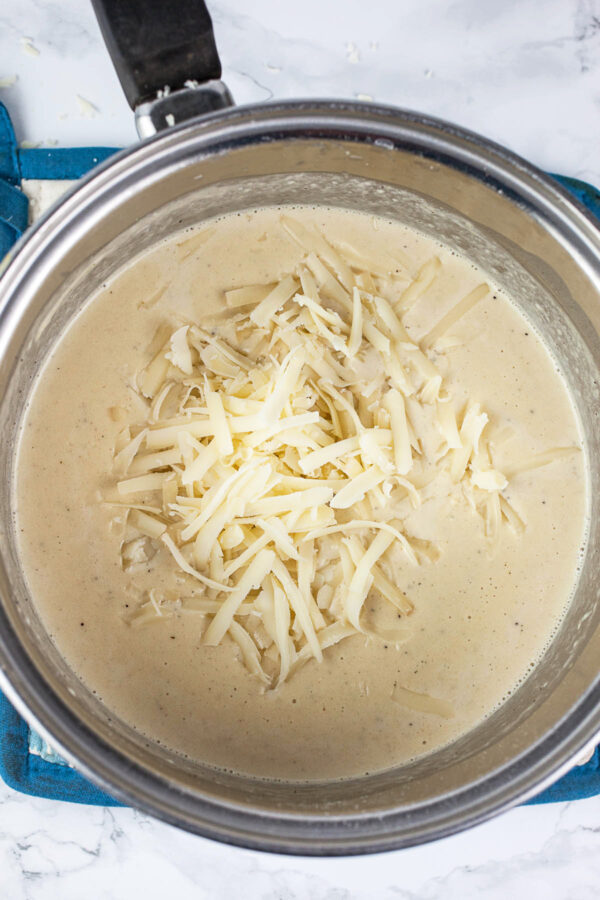 Creamy mixture with shredded Gruyere cheese in sauce pan.