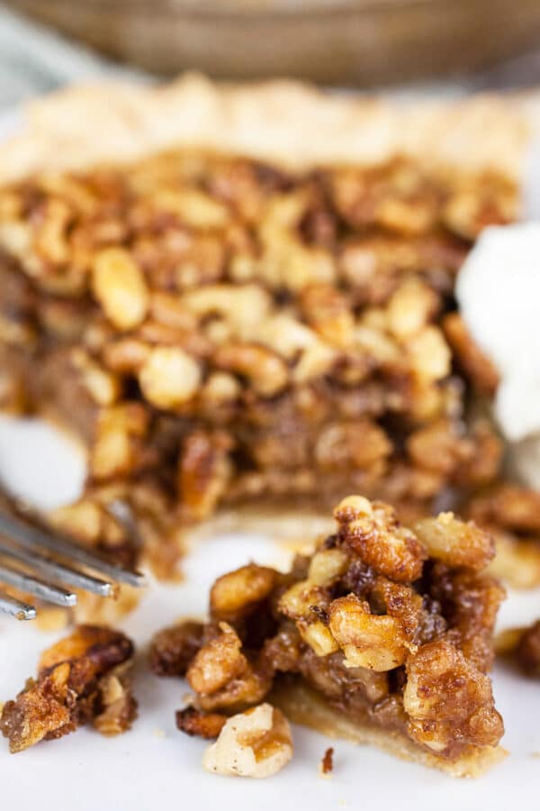 This Maple Bourbon Walnut Pie puts a twist on the traditional pecan pie. It's sweetened with maple syrup and kicked up with a shot of bourbon. This homemade pie is one of my favorite dessert recipes. I will take this maple bourbon walnut pie over pecan any day! #pie #maple #bourbon #walnut #thanksgiving Piece of maple bourbon walnut pie cut with a fork on small white plate.