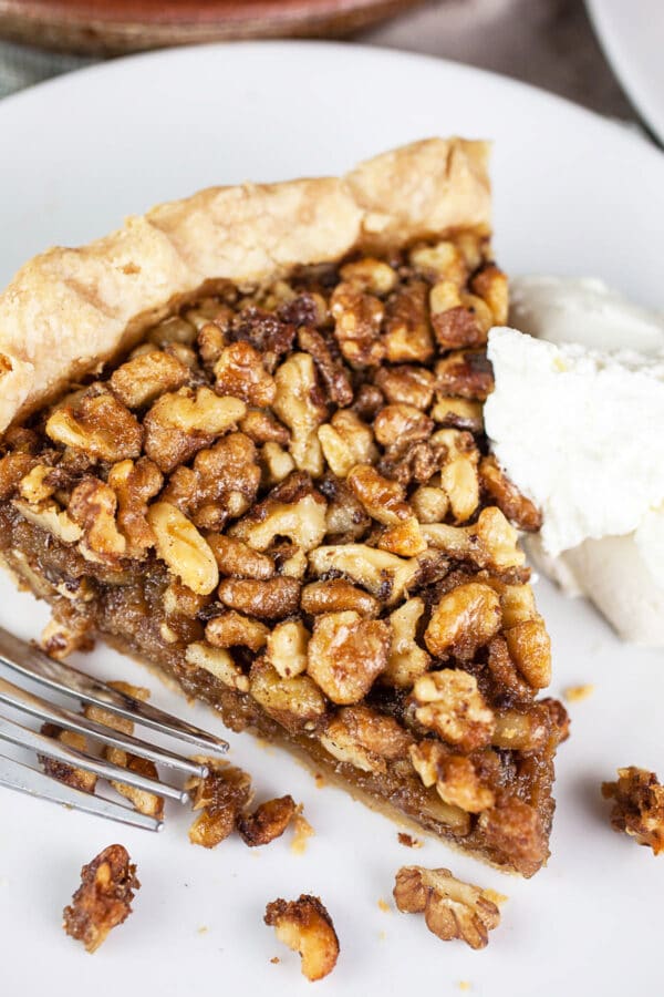 Piece of toasted walnut pie with whipped cream on small white plate with fork.