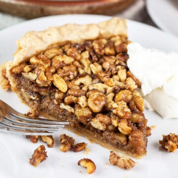 Maple bourbon walnut pie with whipped cream on small white plate with fork.