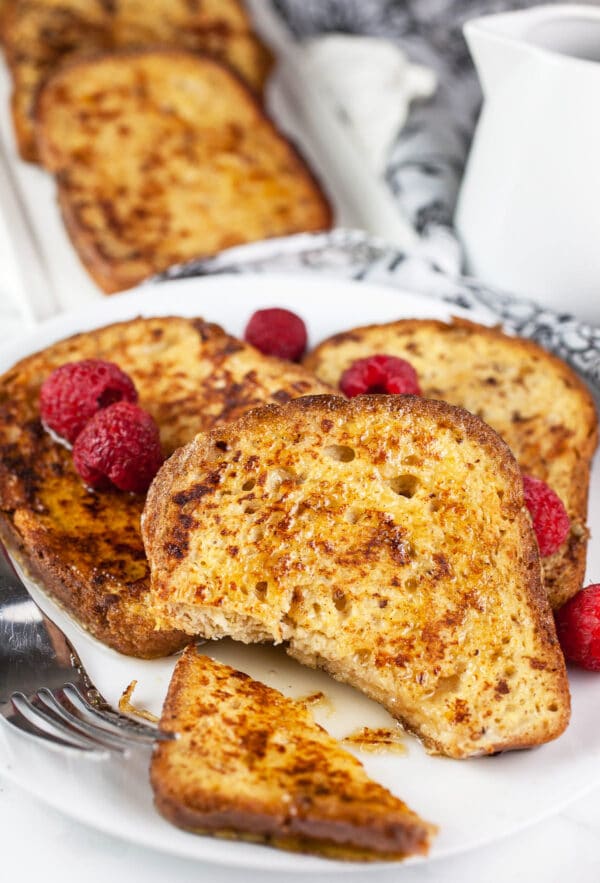 Piece of French toast cut from bread with fresh raspberries on white plate.