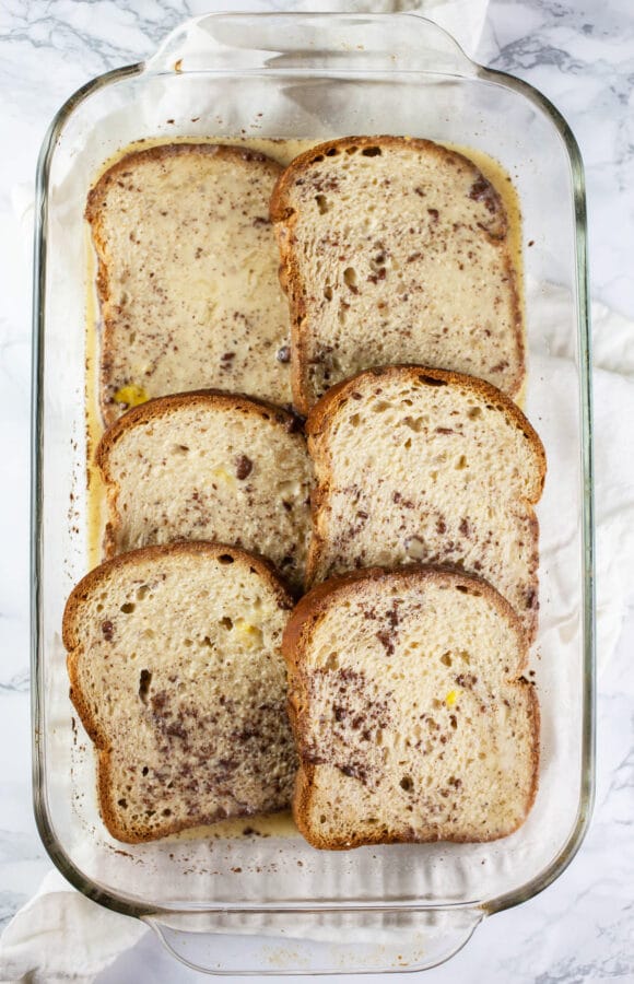 Pieces of bread soaking in egg mixture in small rectangular glass cake pan.