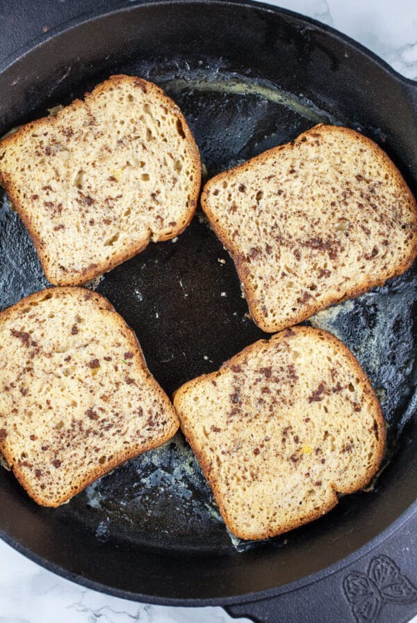 Uncooked bread slices cooking in black cast iron skillet.