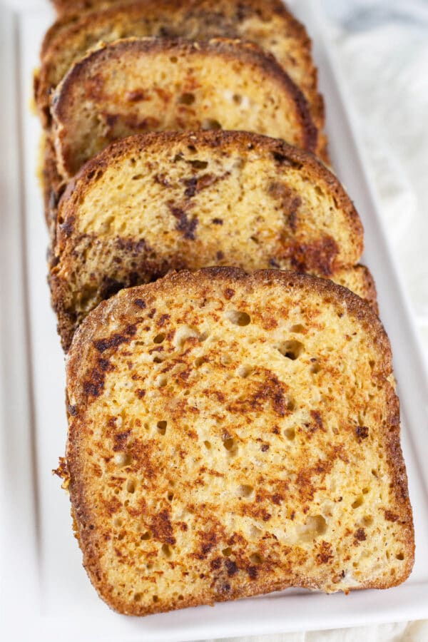 Cooked cardamom French toast slices on white platter.