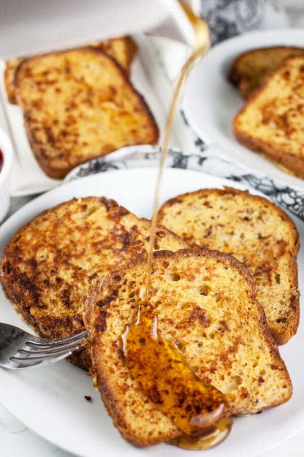 Maple syrup poured onto cardamom French toast on white plate.