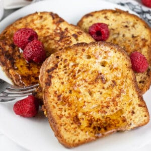 Gluten free skillet cardamom French toast with raspberries on white plate with fork.