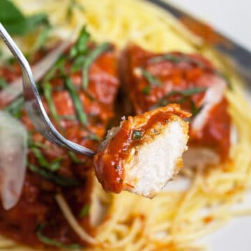 Bite of chicken parmesan on fork lifted from plate.