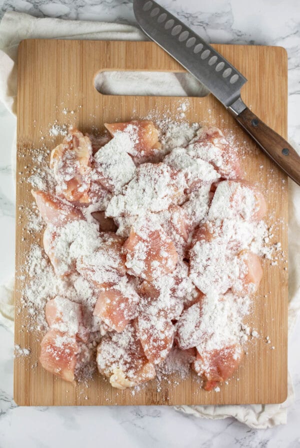 Diced chicken dredged in flour on wooden cutting board.