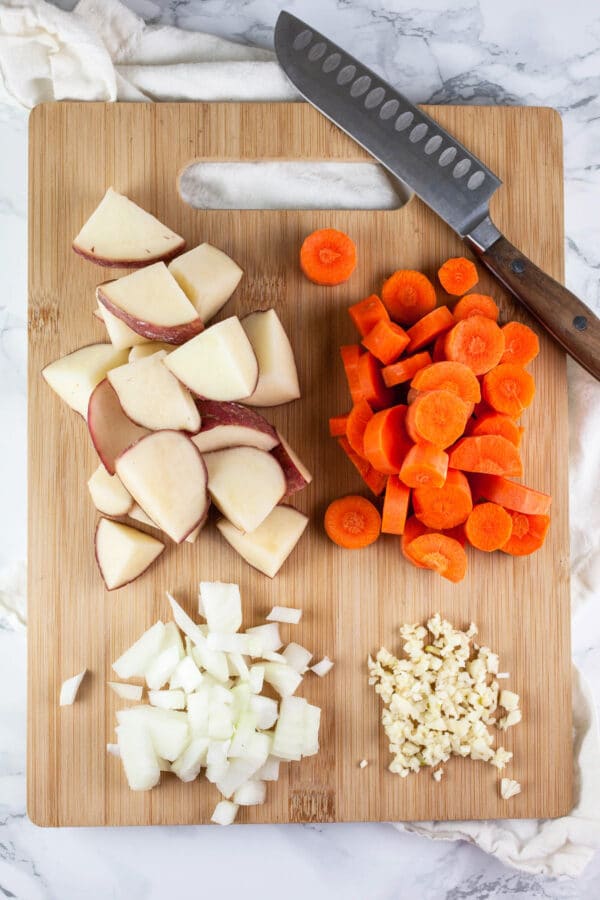 Minced garlic, onions, red potatoes, and carrots on wooden cutting board.