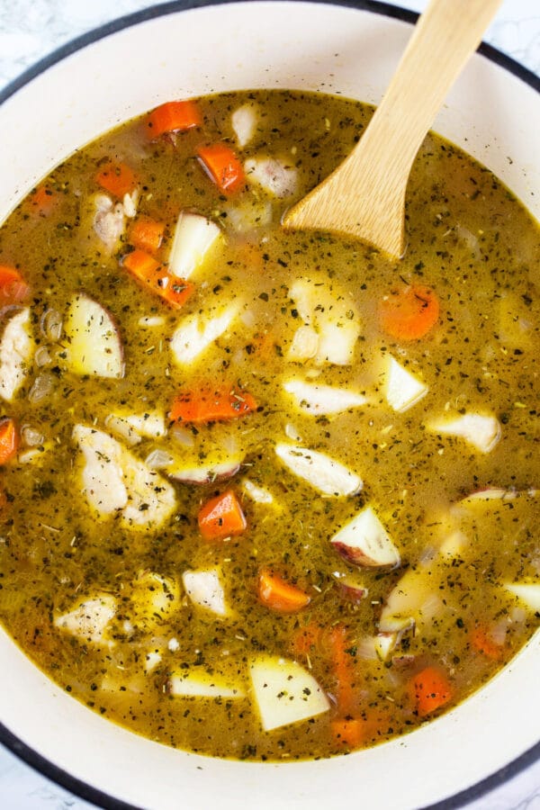 Uncooked chicken stew in white Dutch oven.