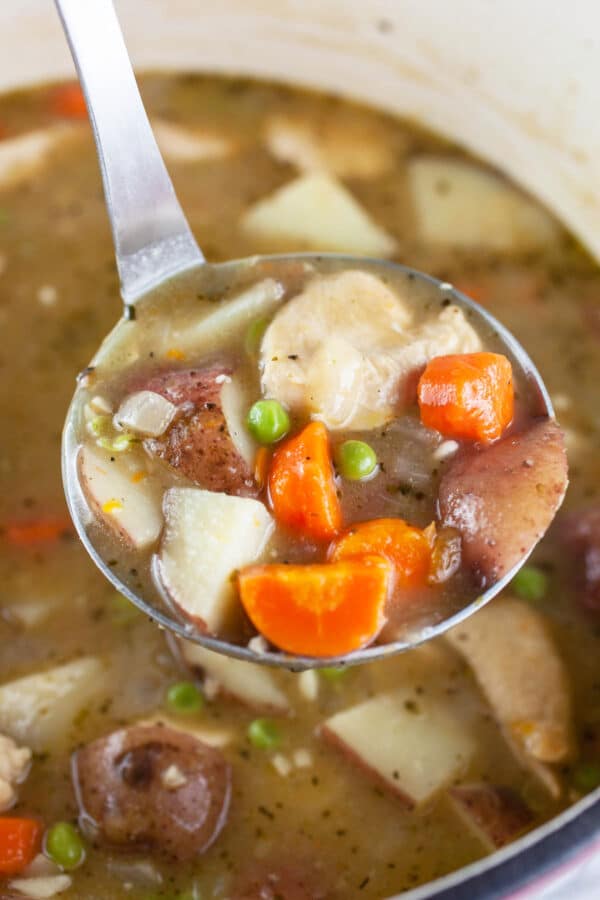 Scoop of gluten free chicken stew lifted from white Dutch oven.