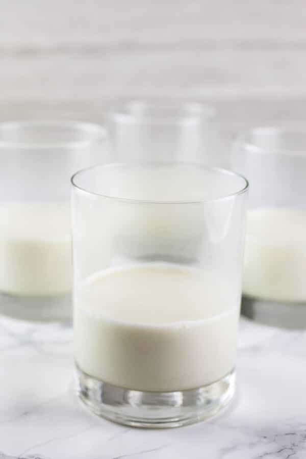 Heavy cream mixture separated into four small glasses on white surface.