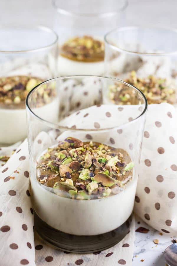 Pistachio panna cotta in four separate glasses with dotted decorative scarf.