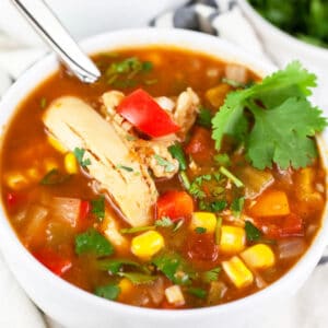 Slow cooker chicken corn soup with cilantro in small white bowl with spoon.