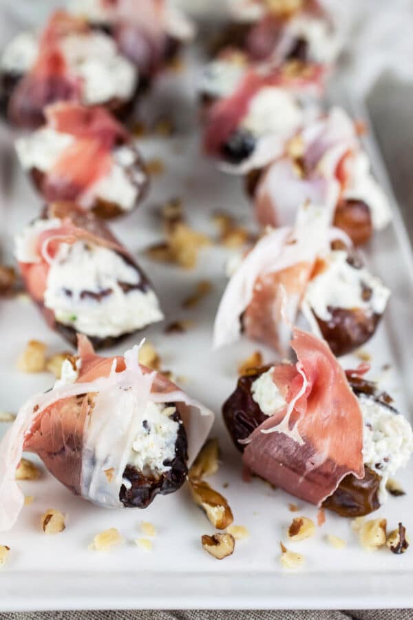 Prosciutto wrapped whipped feta walnut stuffed dates on white platter.