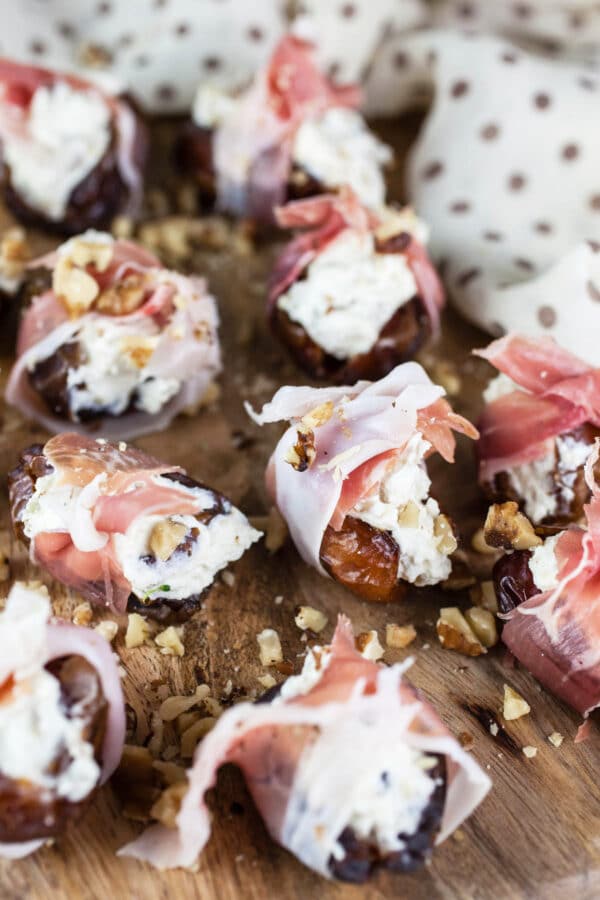 Prosciutto wrapped whipped feta walnut stuffed dates on wooden cutting board.