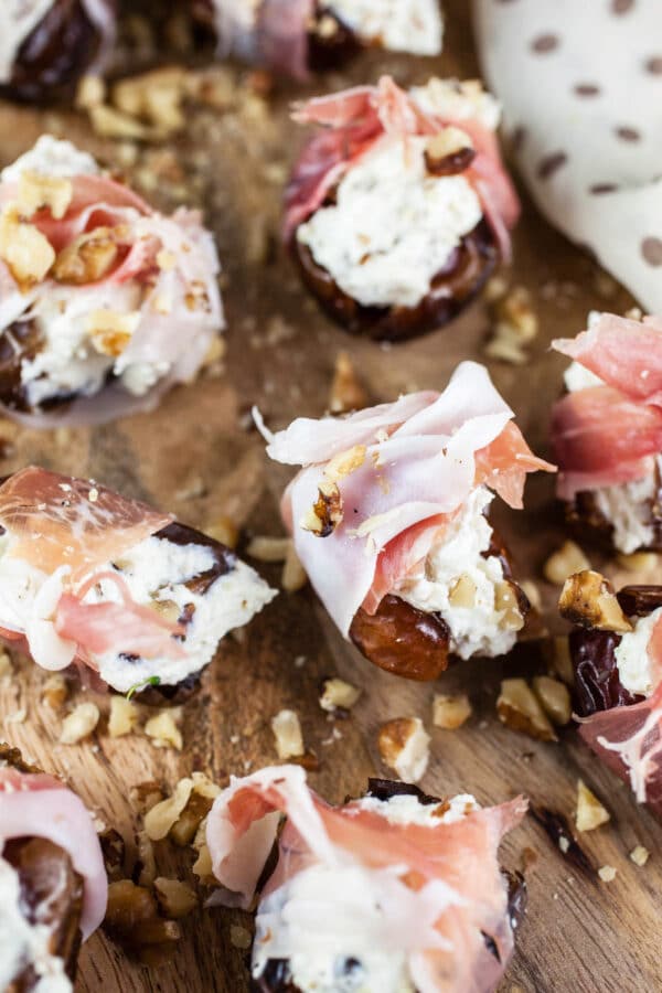 Stuffed dates with whipped feta and prosciutto on wooden cutting board.