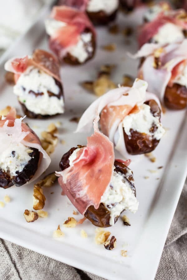 Dates stuffed with feta cheese and wrapped in prosciutto on white serving platter.