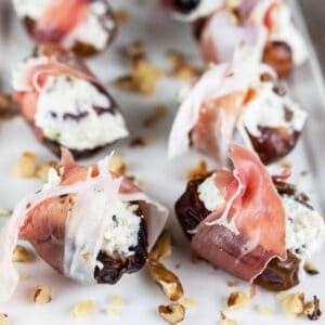 Prosciutto wrapped whipped feta walnut stuffed dates on white platter.