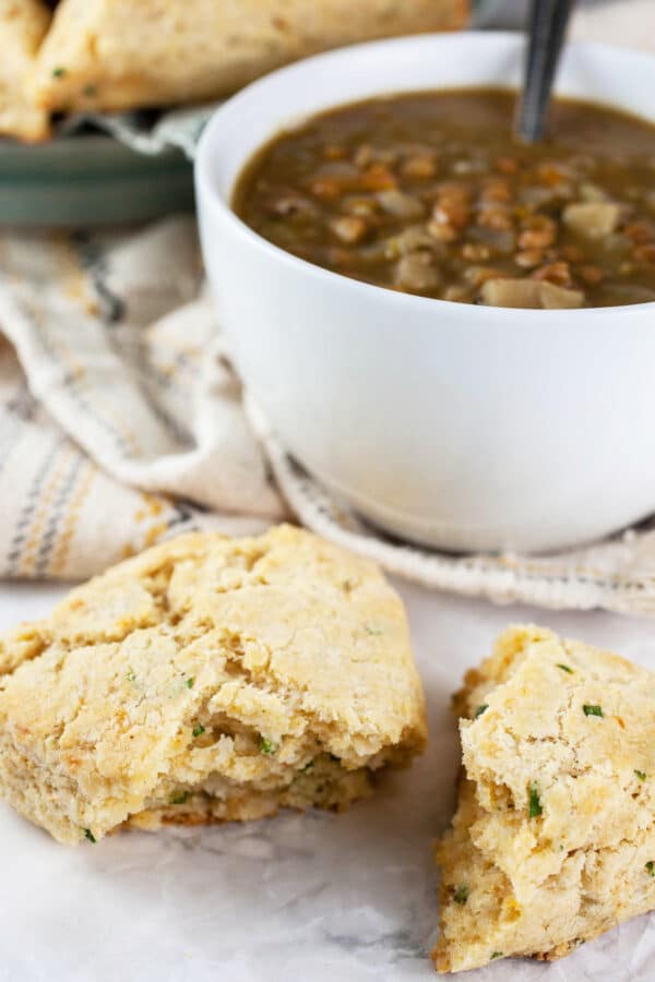 Gluten free cheese scone cut in half in front of white bowl of soup.