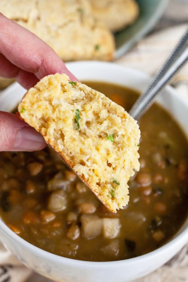 Half of cheddar chive scone dipped into bowl of soup.