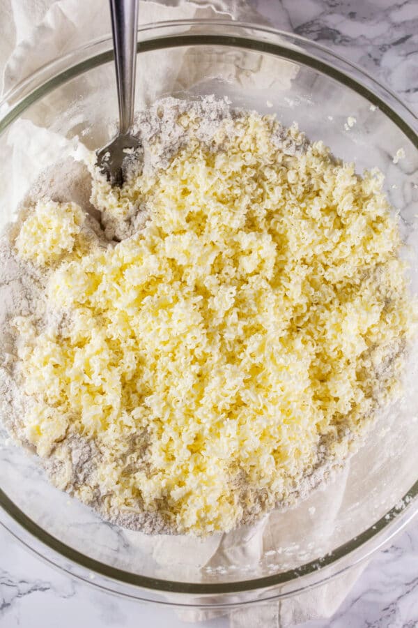 Grated butter added to dry ingredients in glass bowl.