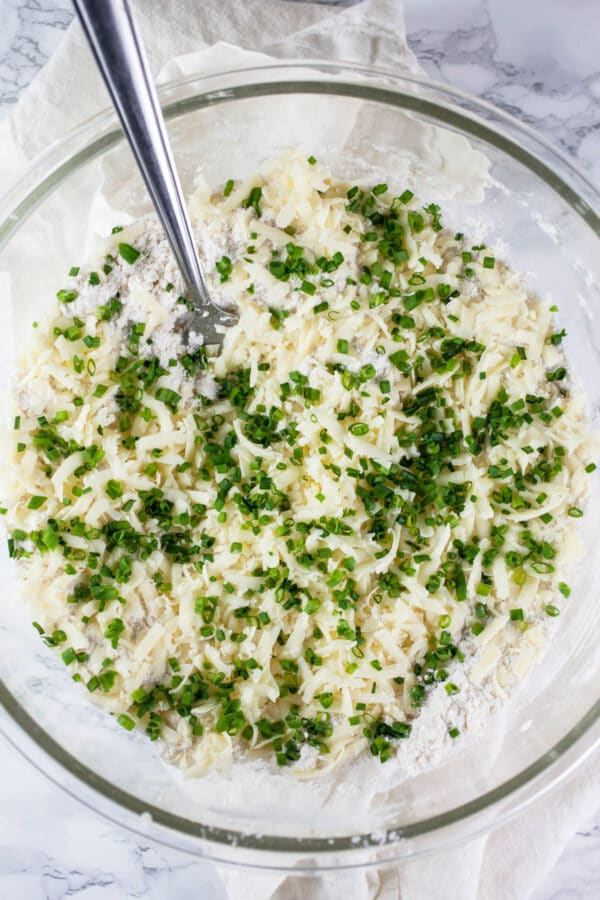 Minced fresh chives added to dry ingredients in glass bowl.