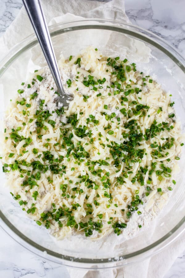 Minced fresh chives added to dry ingredients in glass bowl.