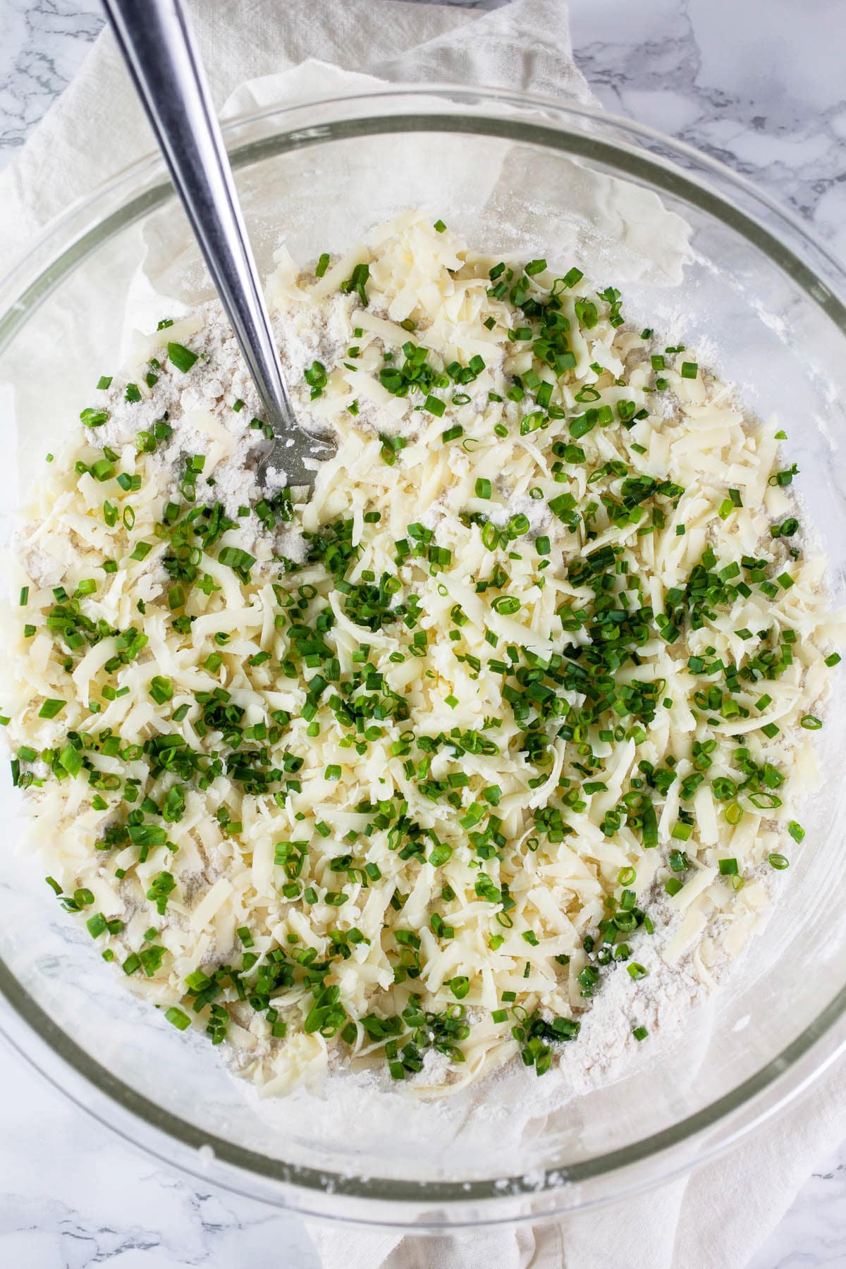 Minced fresh chives added to dry ingredients in glass bowl.