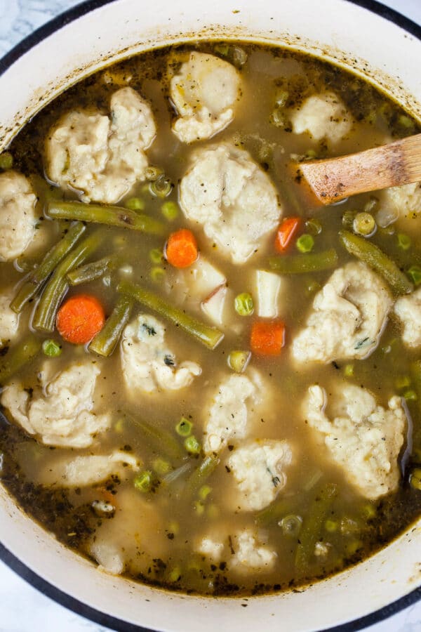 Cooked vegetable stew with dumplings in white Dutch oven.