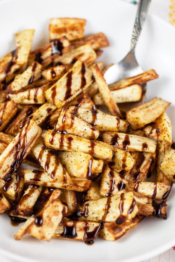 Air fryer parsnips with balsamic glaze in white bowl with spoon.