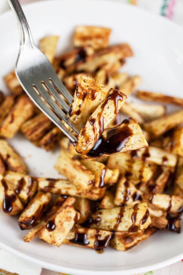 Forkful of air fryer parsnip with balsamic glaze lifted from white bowl.