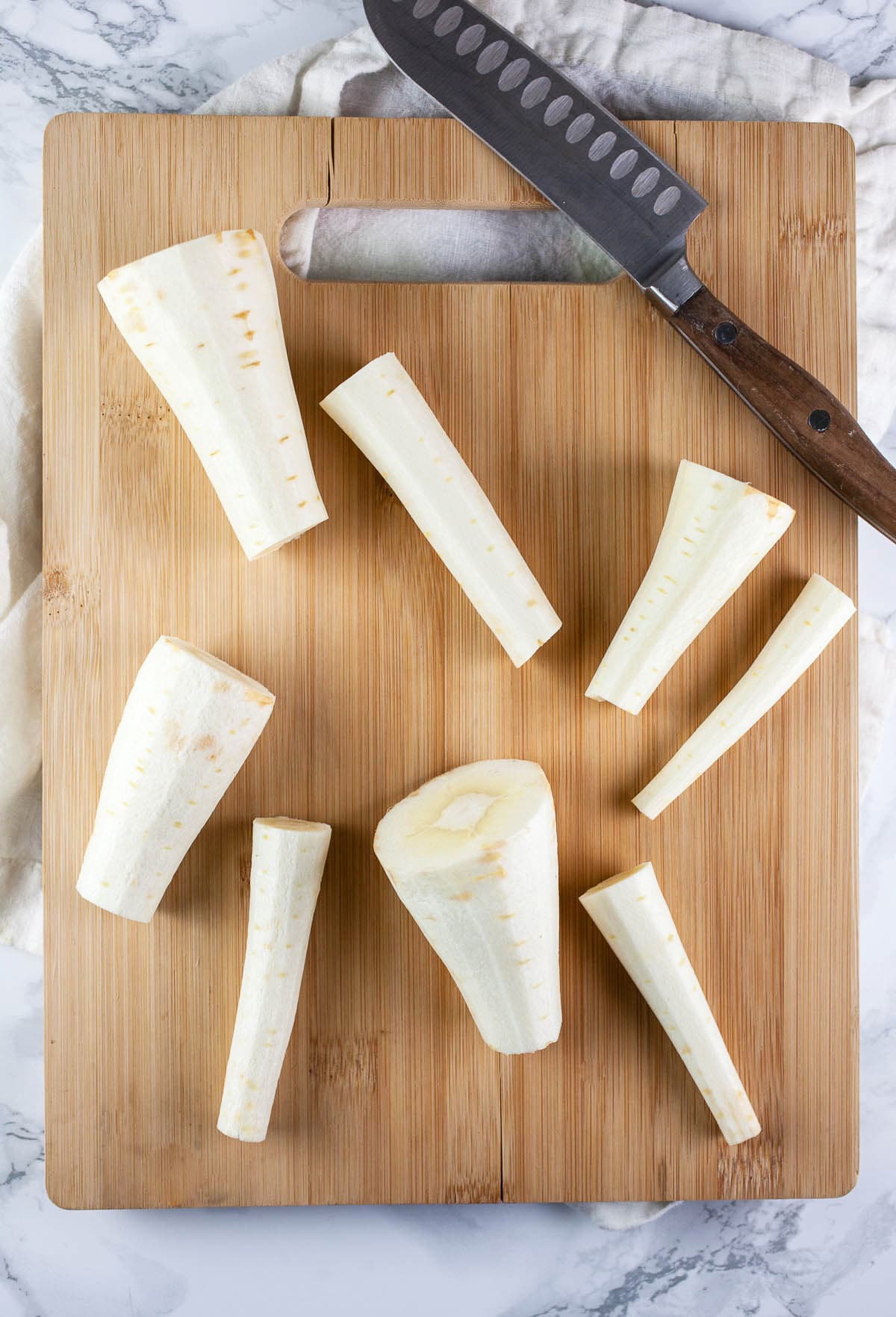 Parsnips cut in half on wooden cutting board with knife.