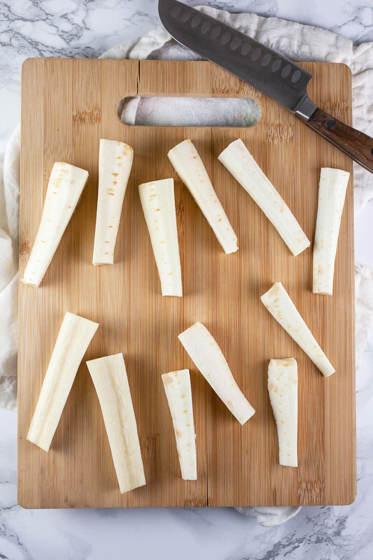 Parsnips cut into strips on wooden cutting board with knife.