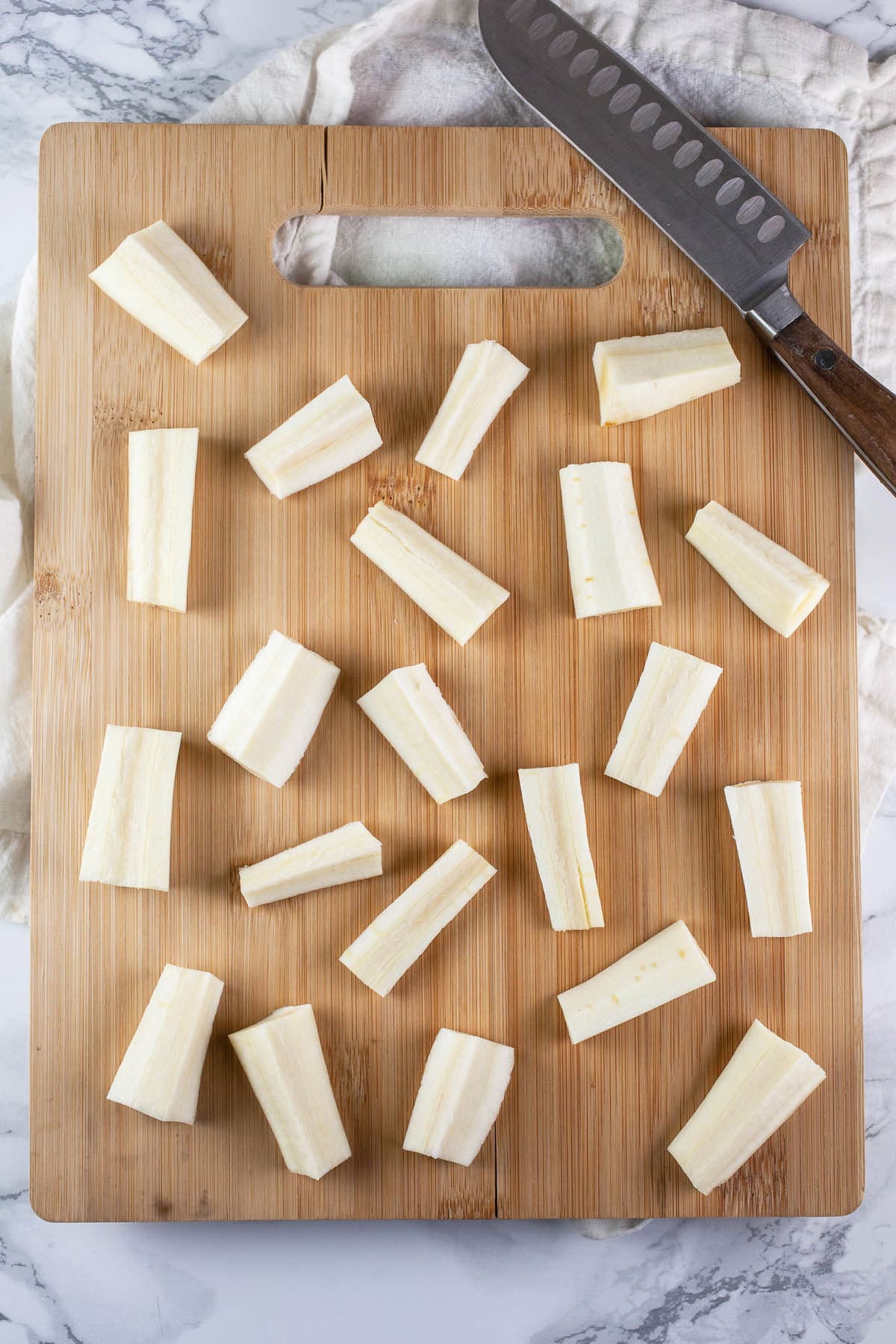 Parsnips cut into chunks on wooden cutting board with knife.