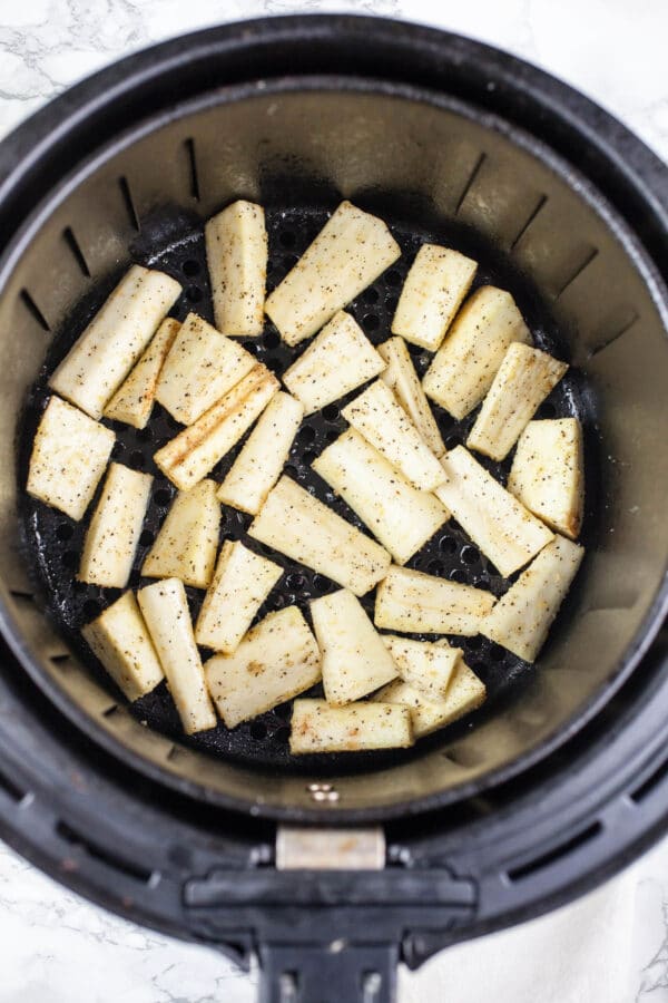 Uncooked parsnips in air fryer basket.