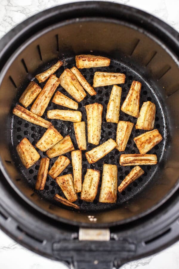 Cooked parsnips in air fryer basket.