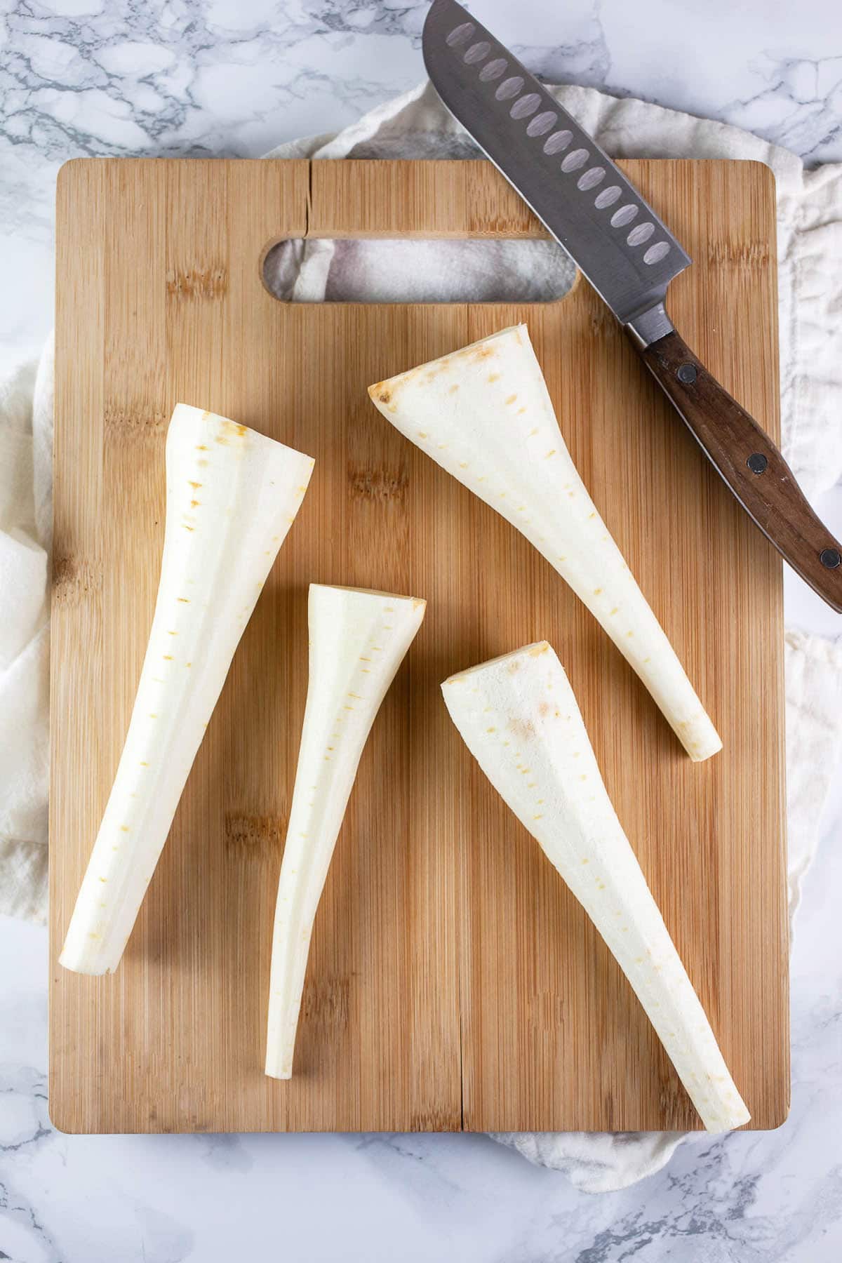 Peeled parsnips on wooden cutting board with knife.