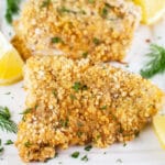 Breaded baked walleye fingers on white platter with lemons and fresh dill.