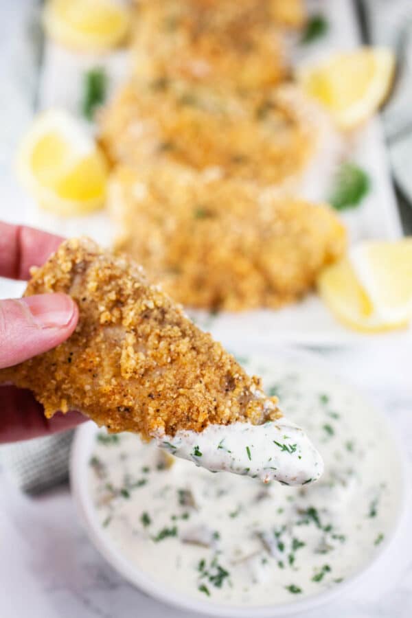 Baked walleye finger dipped into small bowl of tartar sauce.