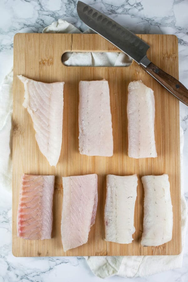 Walleye fish fillets on wooden cutting board with knife.