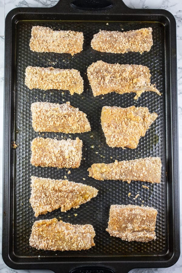 Unbaked fish fillets coated in breadcrumbs on baking sheet.