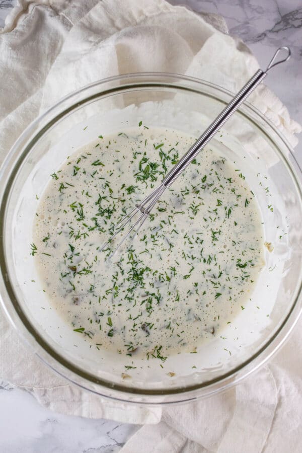 Homemade tartar sauce in small glass bowl with whisk.