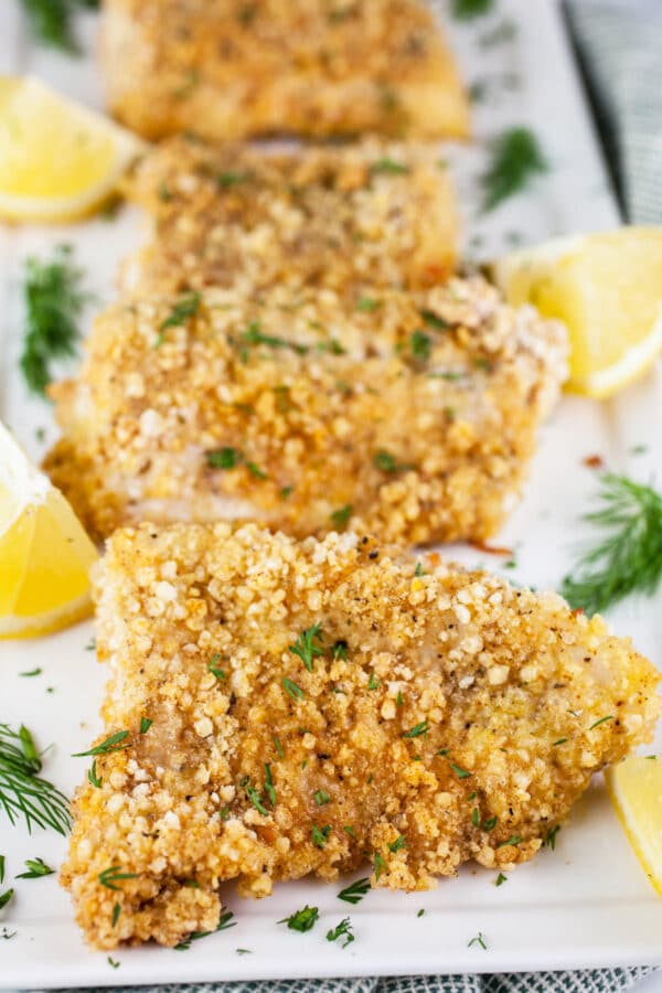 Walleye fingers on white platter with lemon wedges and fresh dill.